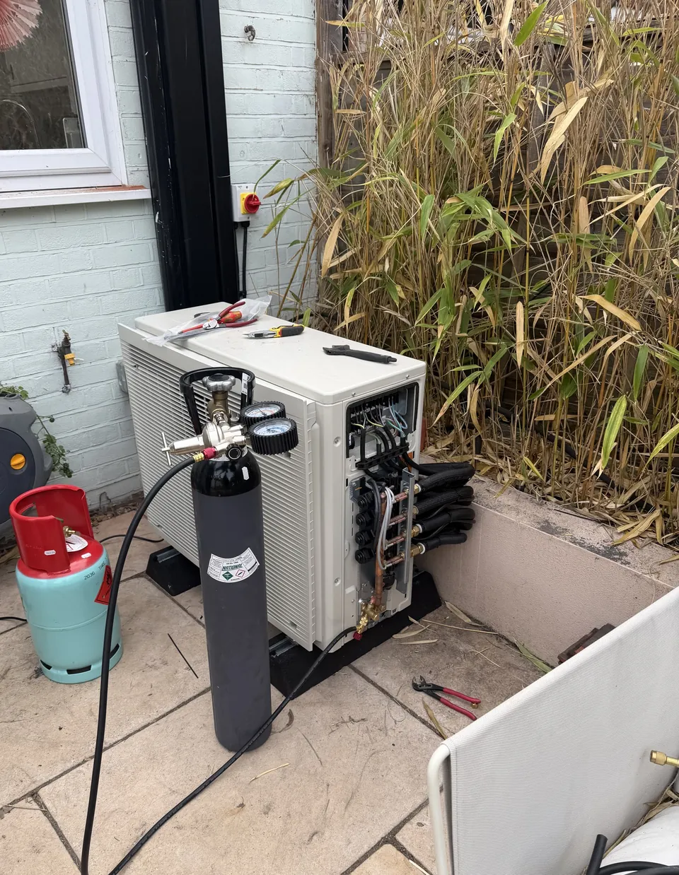 The Daikin outdoor unit on the patio, with the nitrogen cylinder connected for the pressure test.