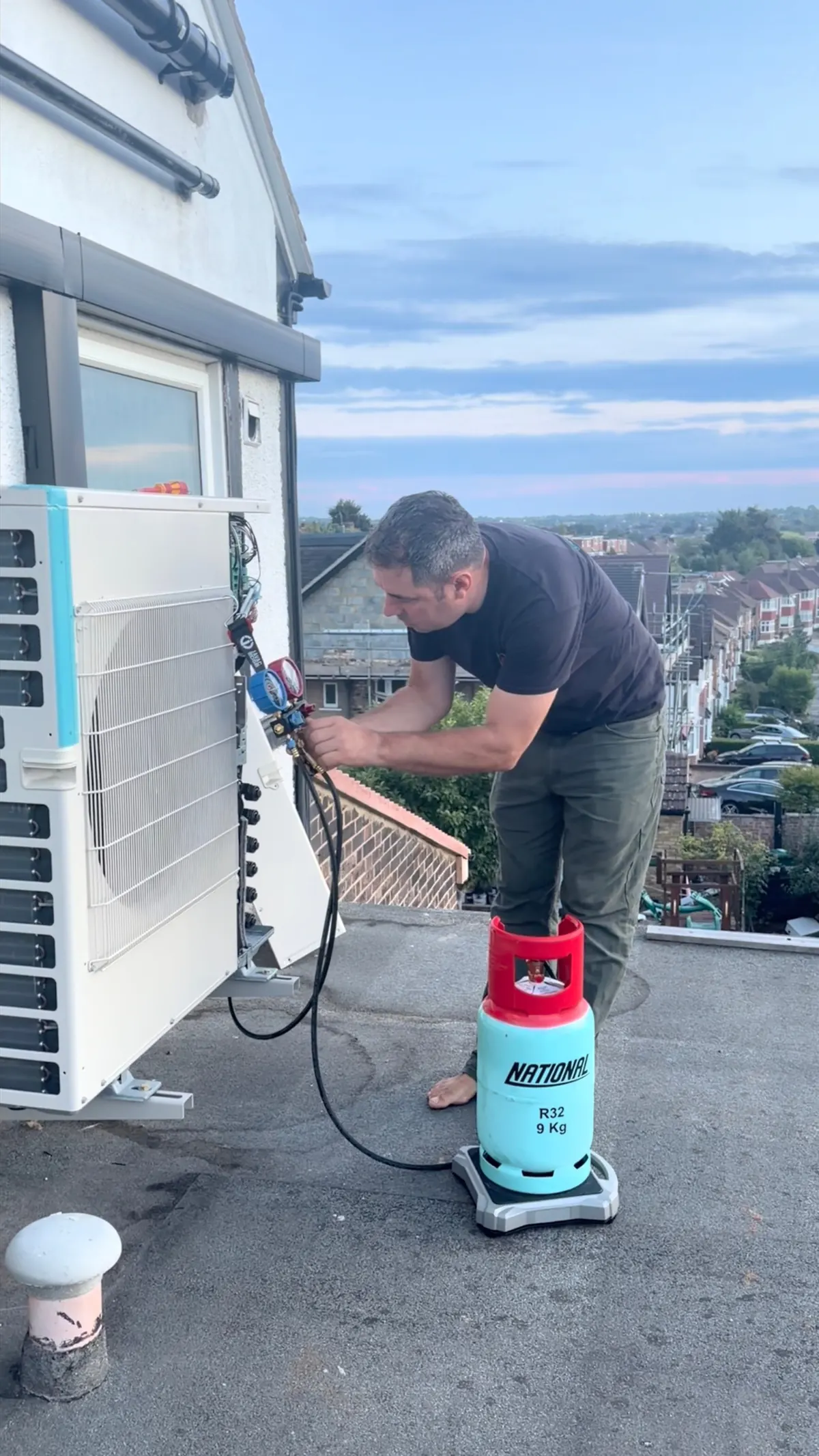 Engineer weighing a refrigerant charge from an R32 cylinder into an air conditioning system on a London roof