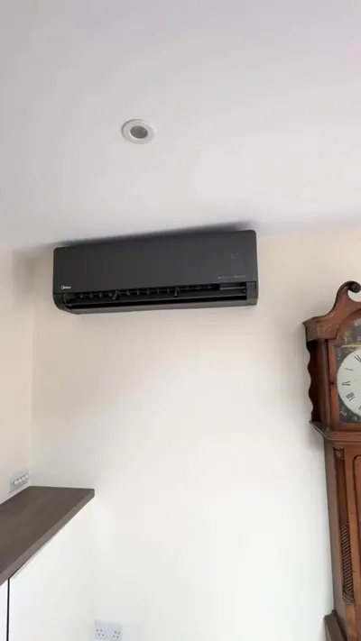 Outdoor unit on a flat roof beside patio doors with refrigerant cylinder and gauges during commissioning