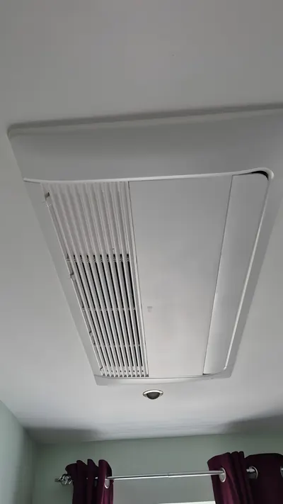 Outdoor unit mounted high on a rendered wall with a ladder alongside