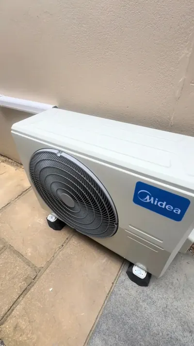 Finished Midea outdoor unit standing on paving slabs beside a house wall