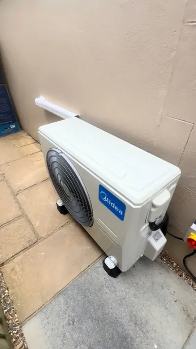 Ceiling cassette air conditioning unit recessed into a white ceiling next to a downlight